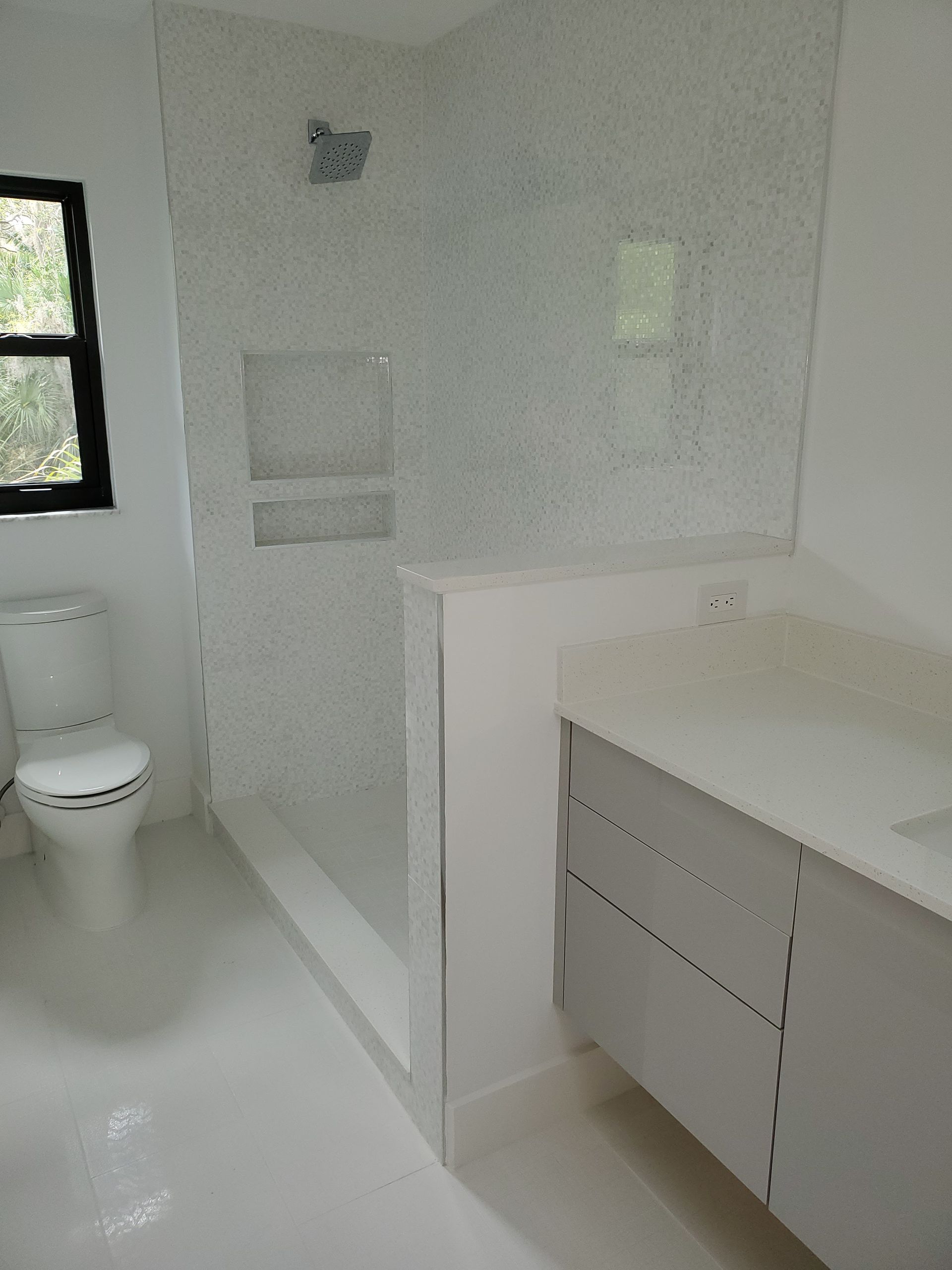 Modern bathroom with a white toilet, a grey vanity with white countertop, and a walk-in shower with tiled walls.