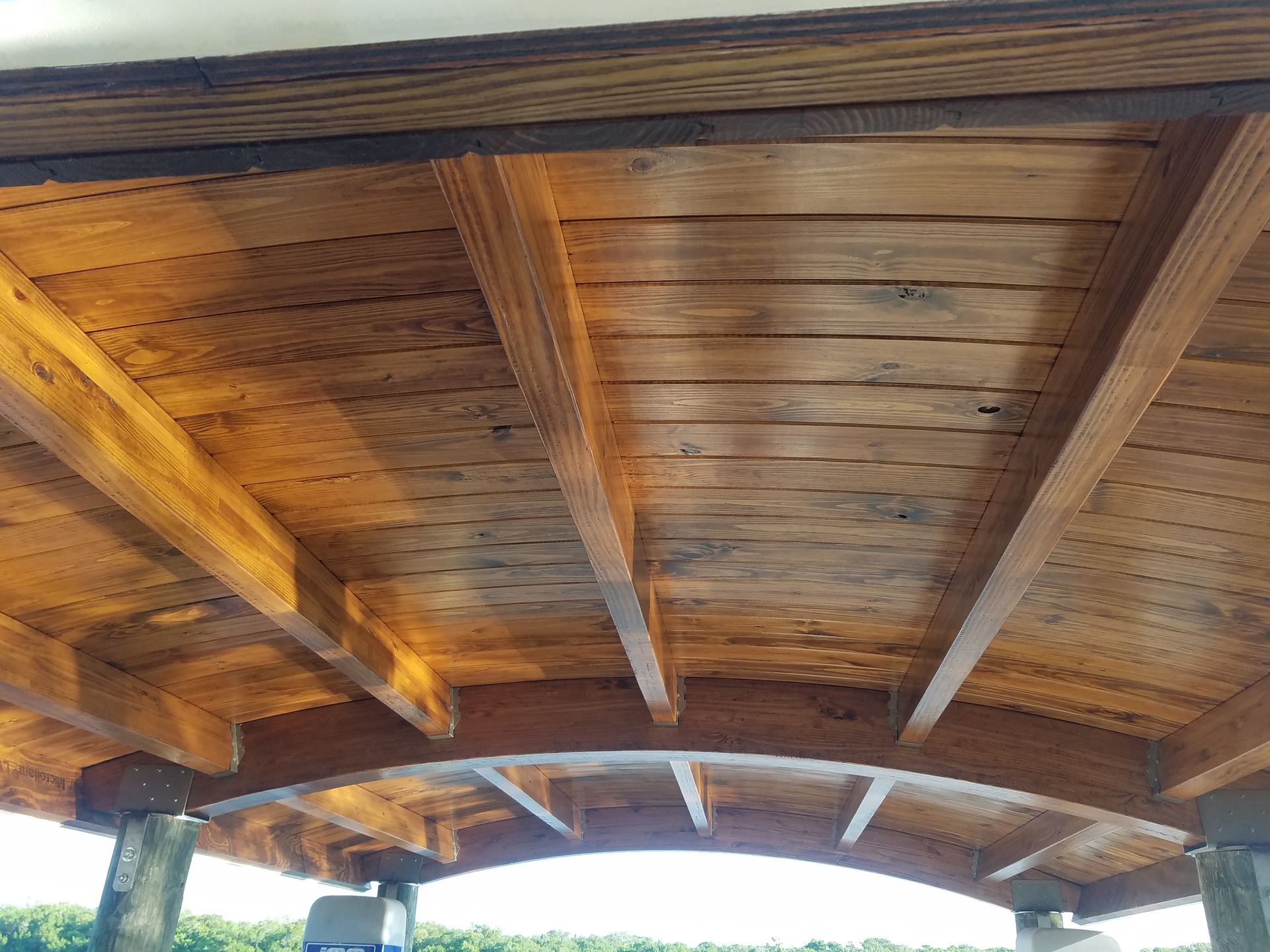 Underside of a wooden dock roof with visible beams and planking, showing a curved design over a body of water.
