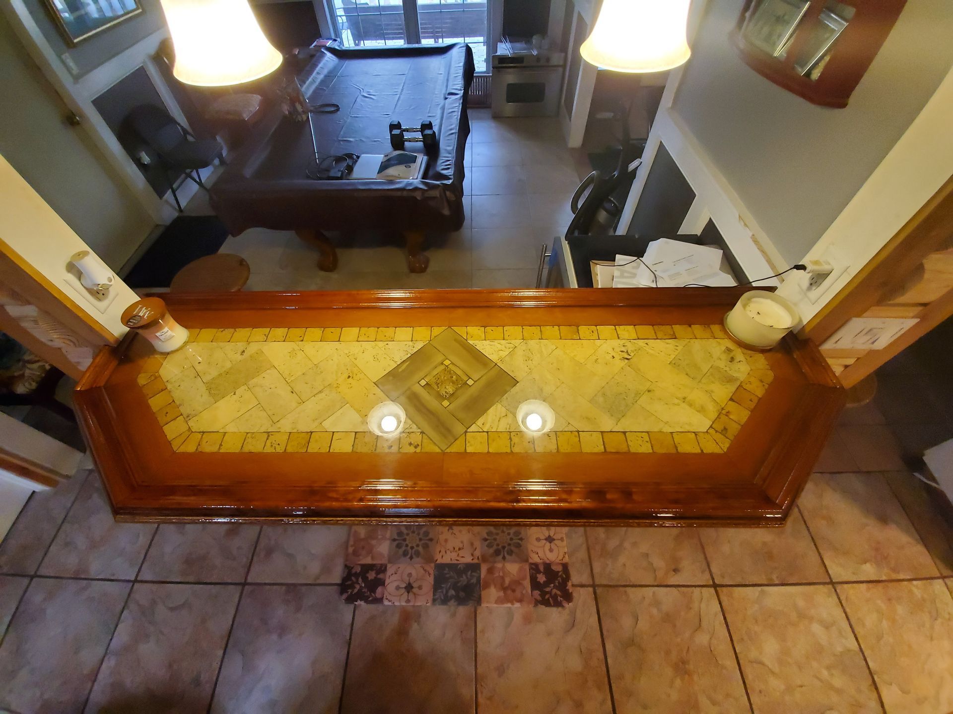 A bar counter with a yellow tiled top and wood trim, overlooking a room with a pool table, viewed from above.