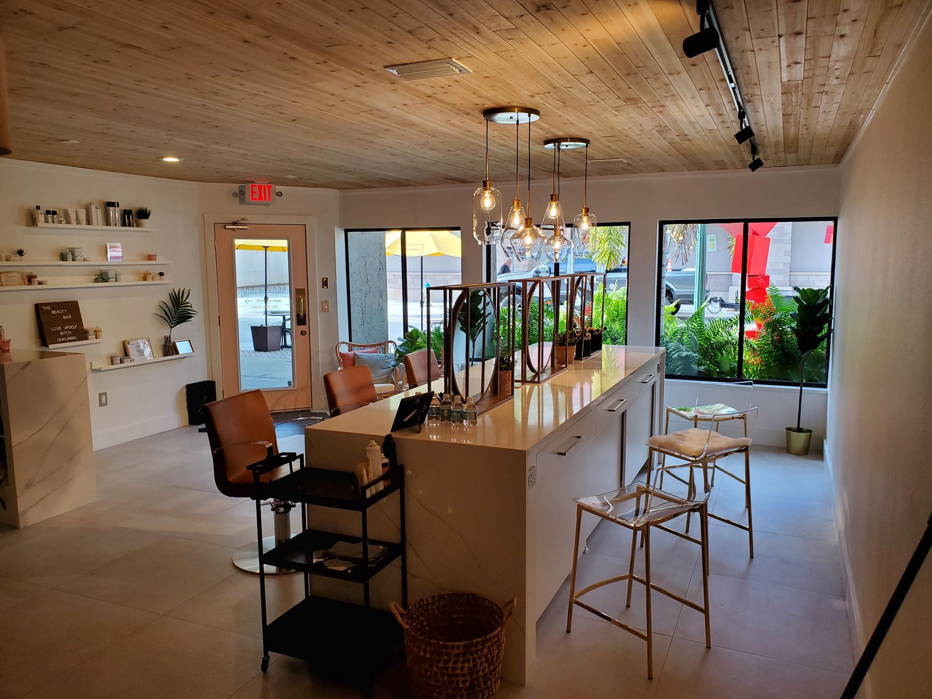 A brightly lit, minimalist salon interior featuring a central white service counter with tall stools and pendant lights.