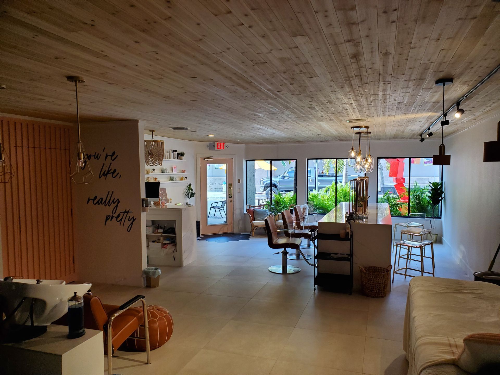 Modern hair salon with light wood ceiling, minimalist decor, white styling stations, and wall text reading 