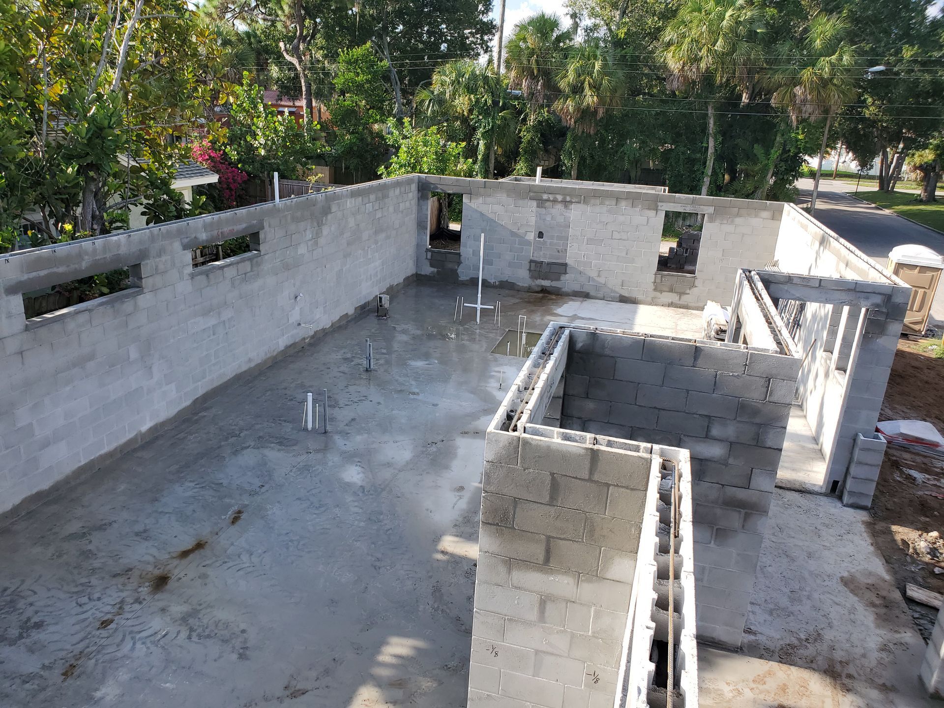 An aerial view of a concrete building under construction with exposed gray cinder block walls and interior plumbing pipes.