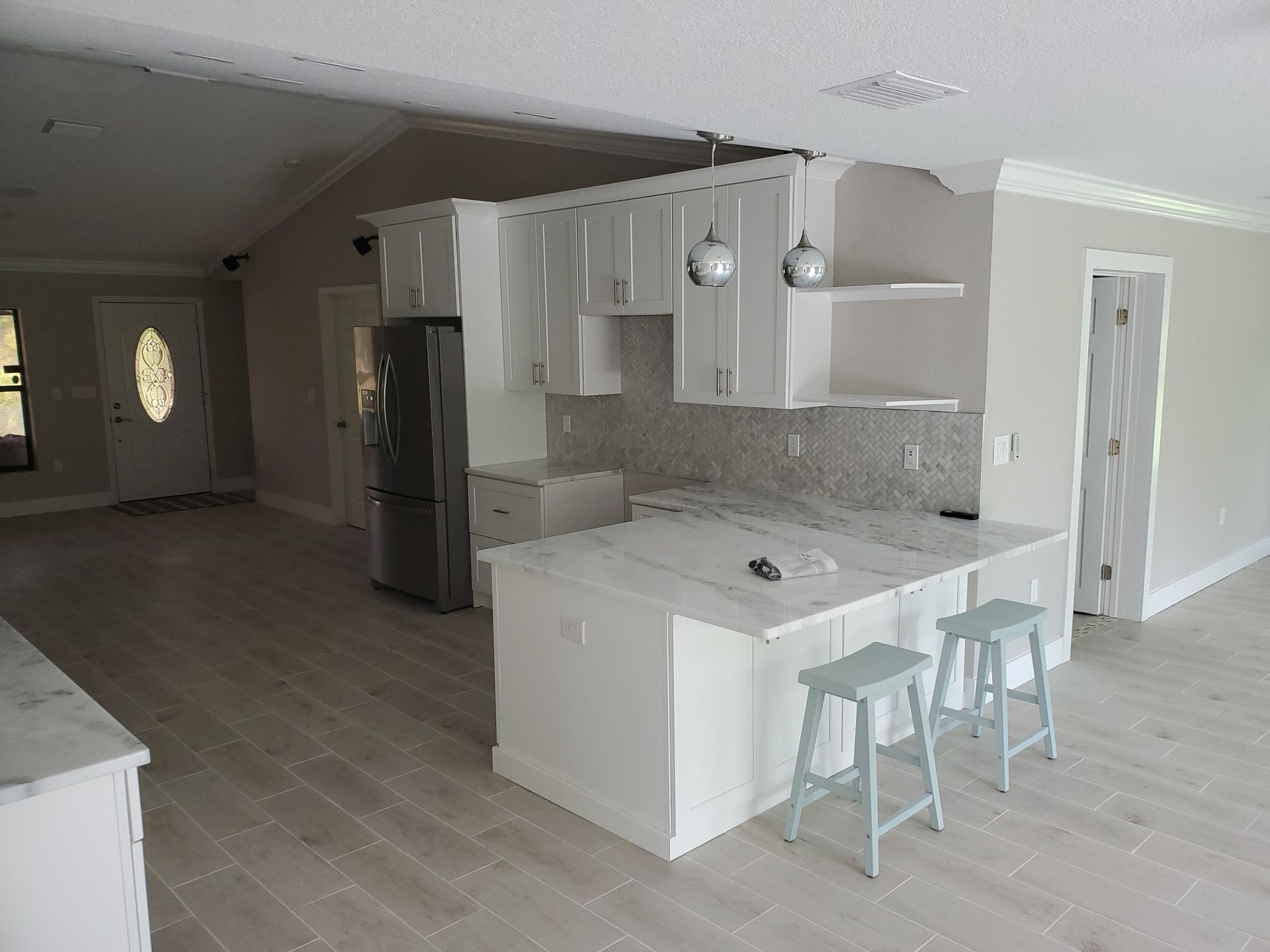 A modern kitchen with a white island, two light blue stools, white cabinetry, and stainless steel appliances.