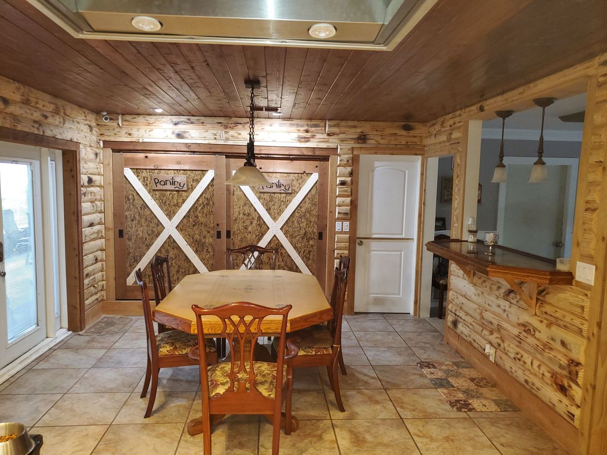 A rustic dining room featuring a wooden table, chairs, barn-style wall decor, and a wooden bar counter.