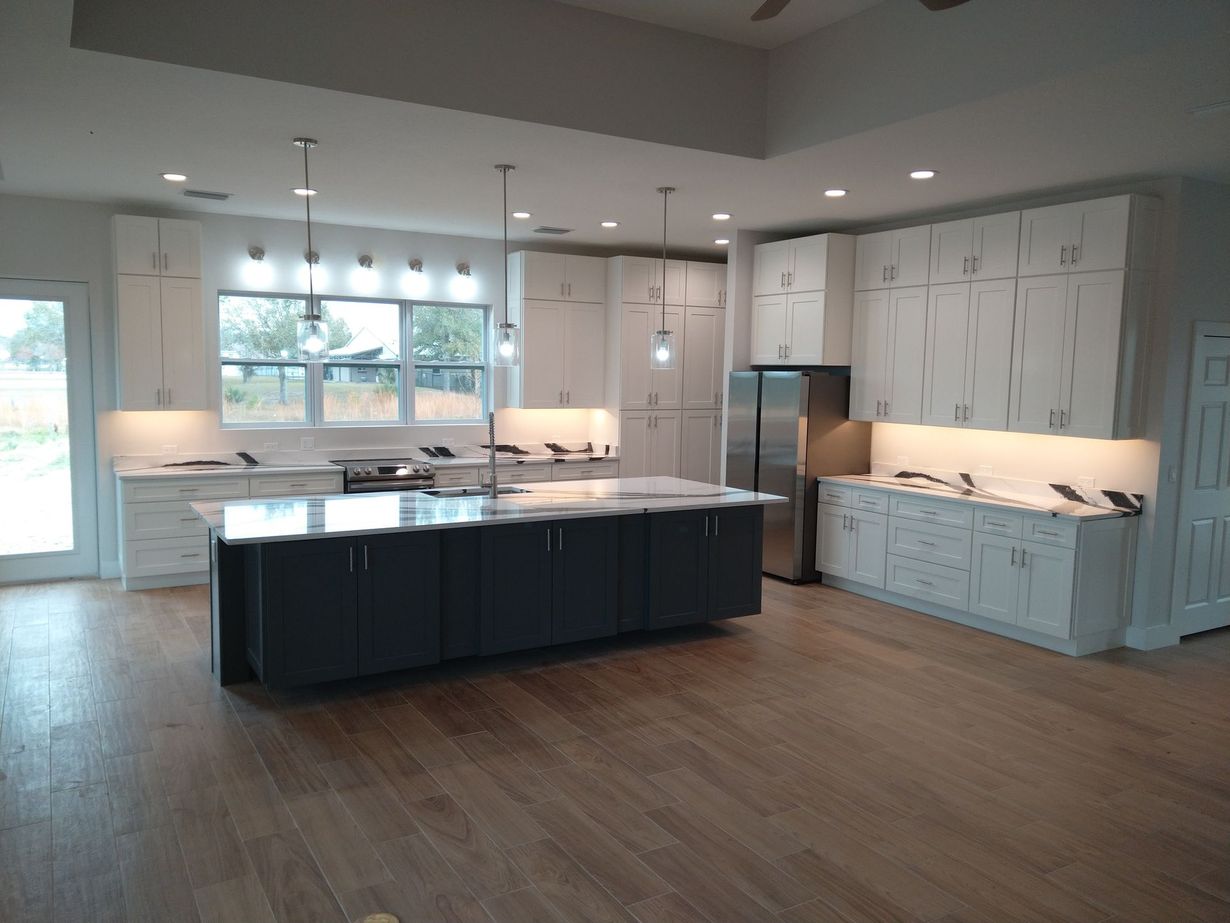 A modern kitchen featuring white cabinets, a large dark gray island with granite countertops, and light wood flooring.