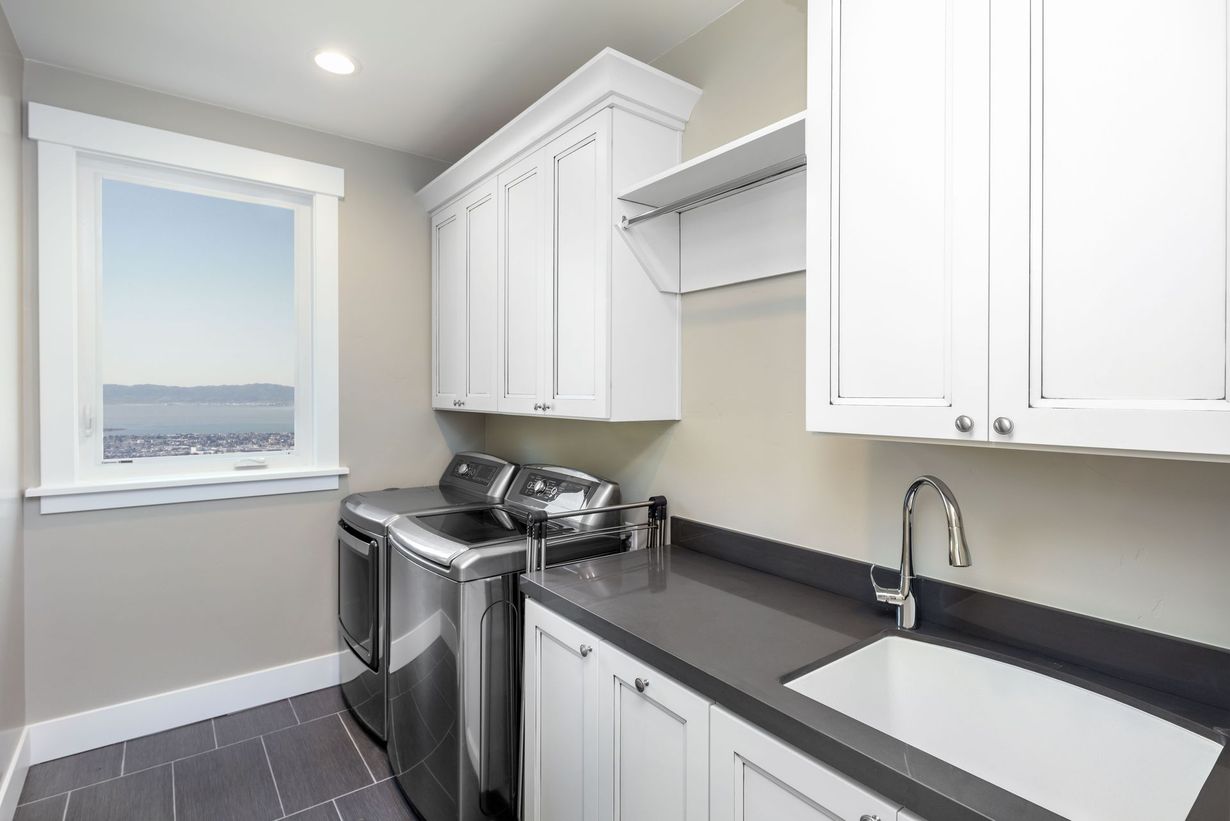 A laundry room featuring stainless steel appliances, white cabinetry, a sink with a faucet, and gray tiled floors.