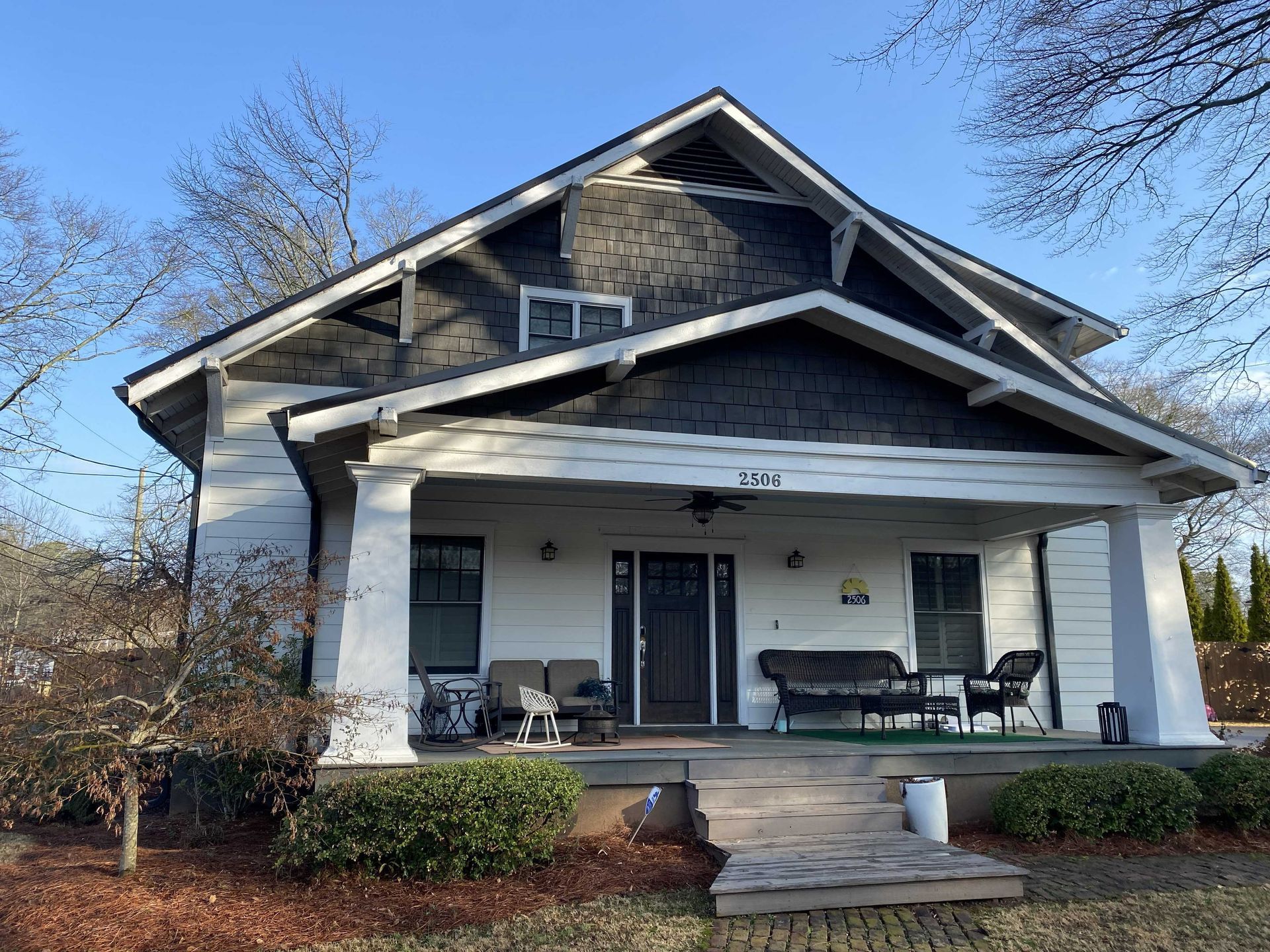 Small house with a covered front porch, white columns, and steps leading up from a yard.