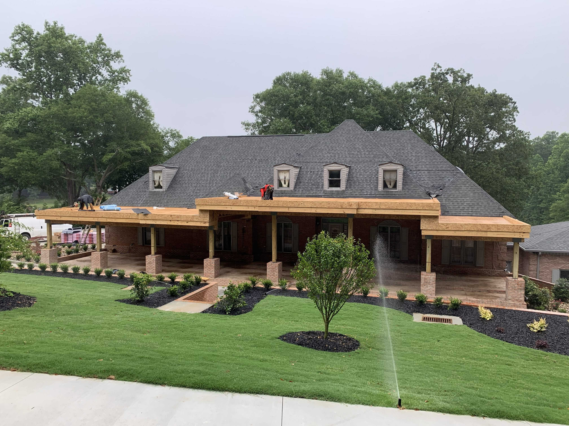Stone house with gray roof, covered porch, and manicured lawn with sprinklers in front