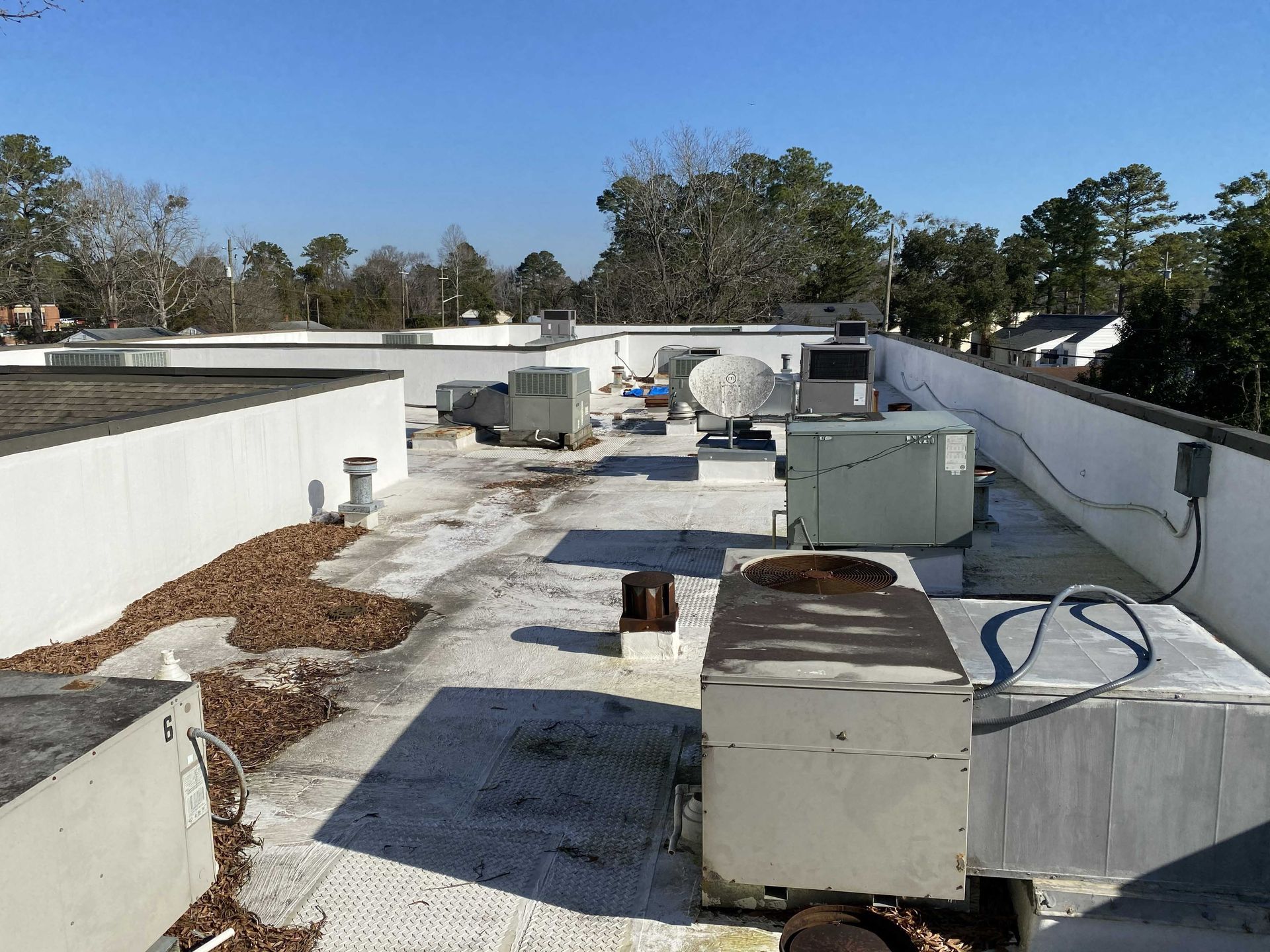 Flat rooftop with HVAC units, ducts, and scattered leaves under a clear sky.