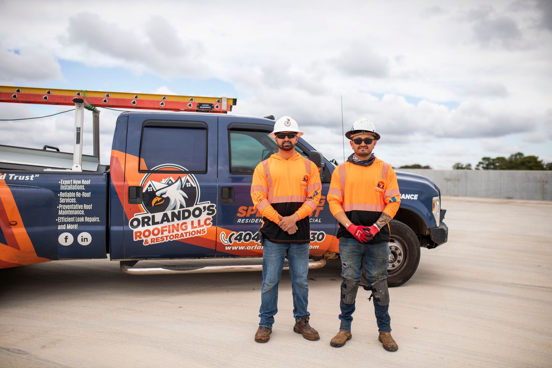 Two road workers in orange safety gear stand beside a black utility truck on a concrete roadway.