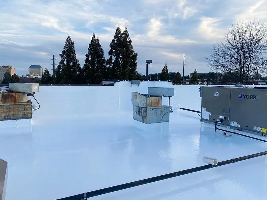 Rooftop with white waterproof membrane, HVAC units, and trees under a cloudy sky.