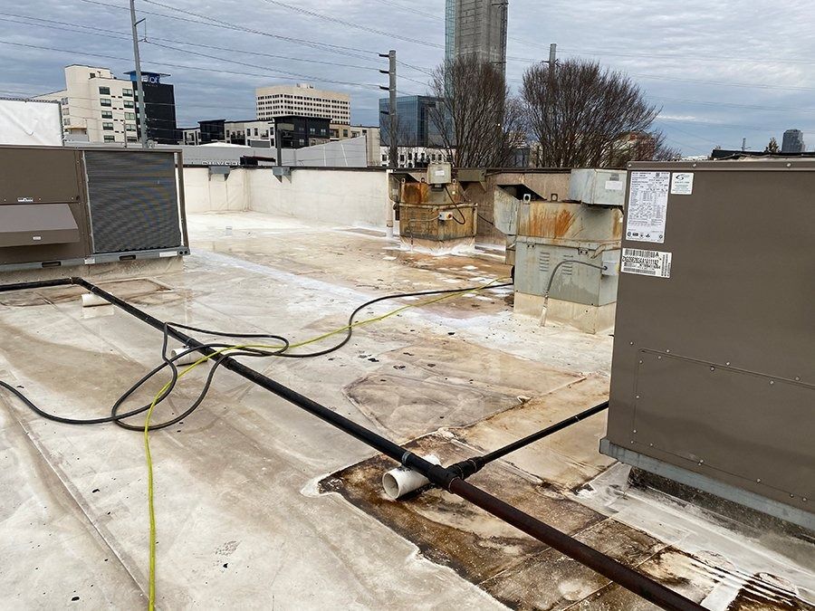 Flat rooftop with HVAC units, cables, and water puddles under a cloudy sky