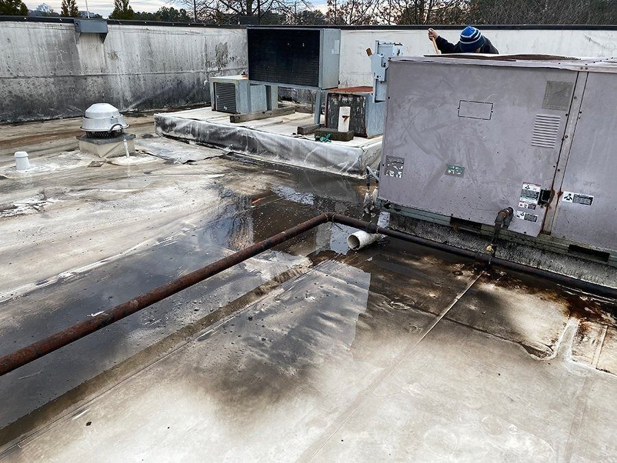 Rooftop with large gray HVAC units, wet concrete, and a rusted pipe crossing the surface.