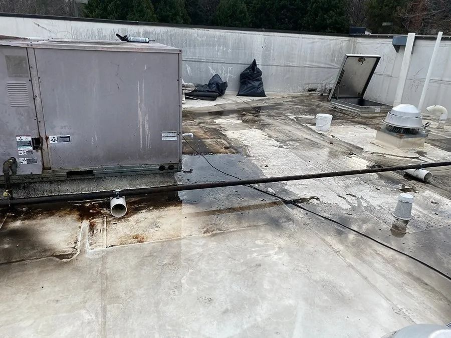 Rooftop with HVAC units, white parapet walls, scattered debris, and weathered concrete surface