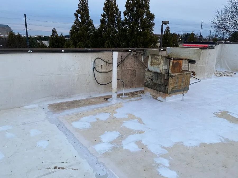 Rooftop with white waterproof coating, pipes, and a small utility unit near the parapet.