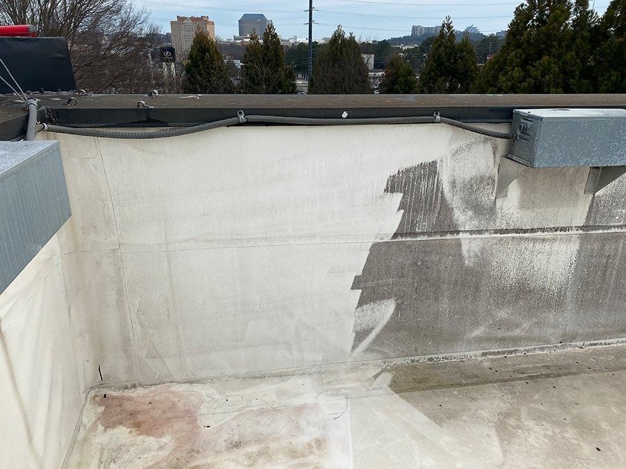 Rooftop concrete wall with weathered stains and a black railing, overlooking trees and buildings.