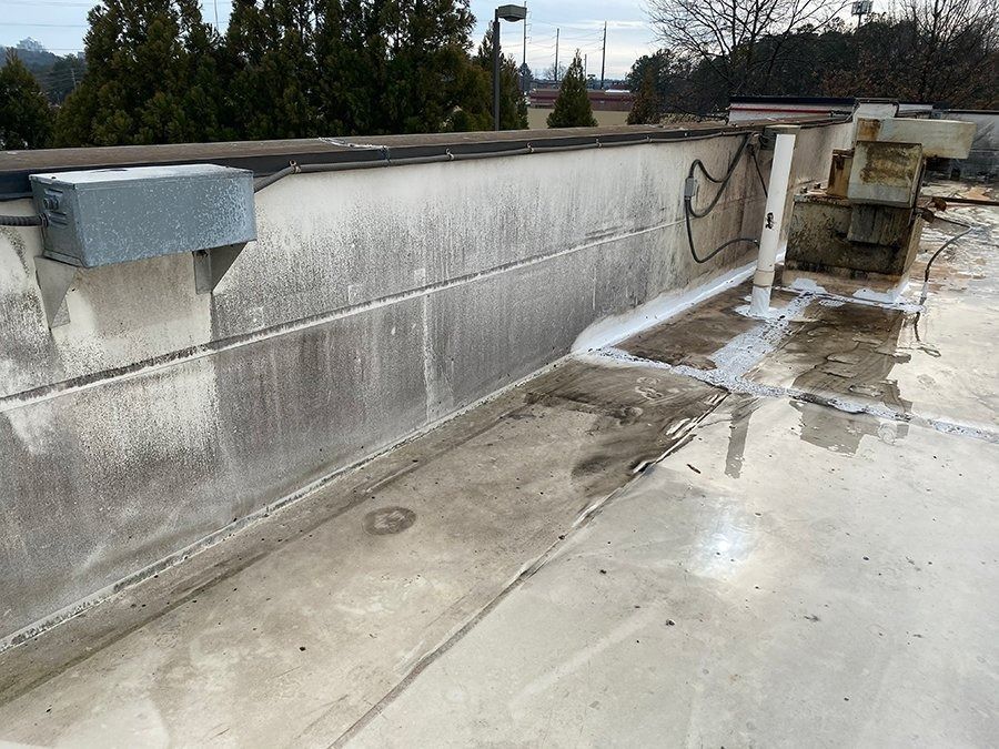 Rooftop with concrete parapet wall, wet surface, and drainage pipes on a cloudy day