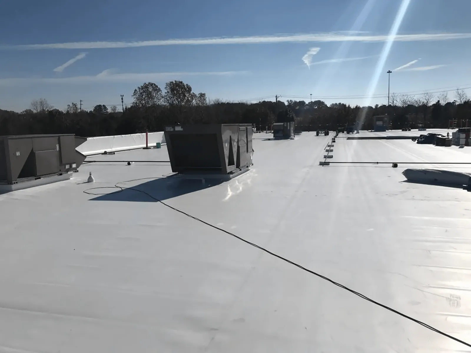 Snow-covered flat rooftop with vents and equipment under a bright blue sky