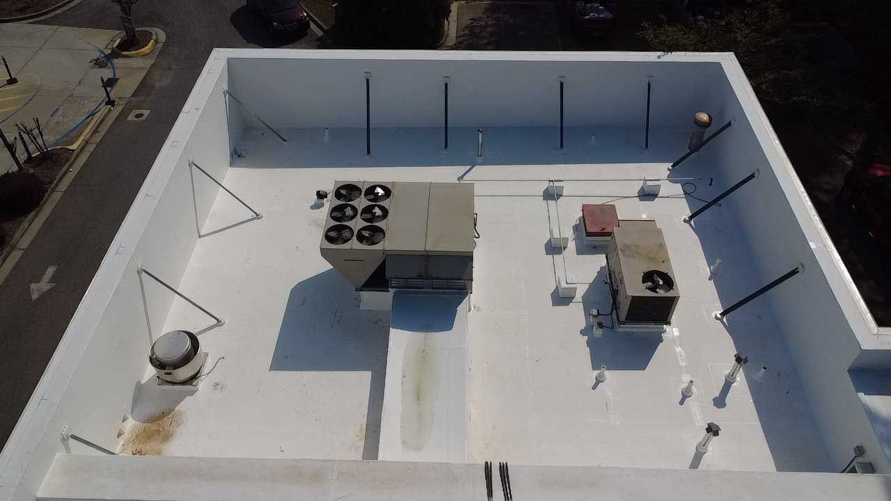 Rooftop with white walls, HVAC units, vents, and pipes under bright sunlight.
