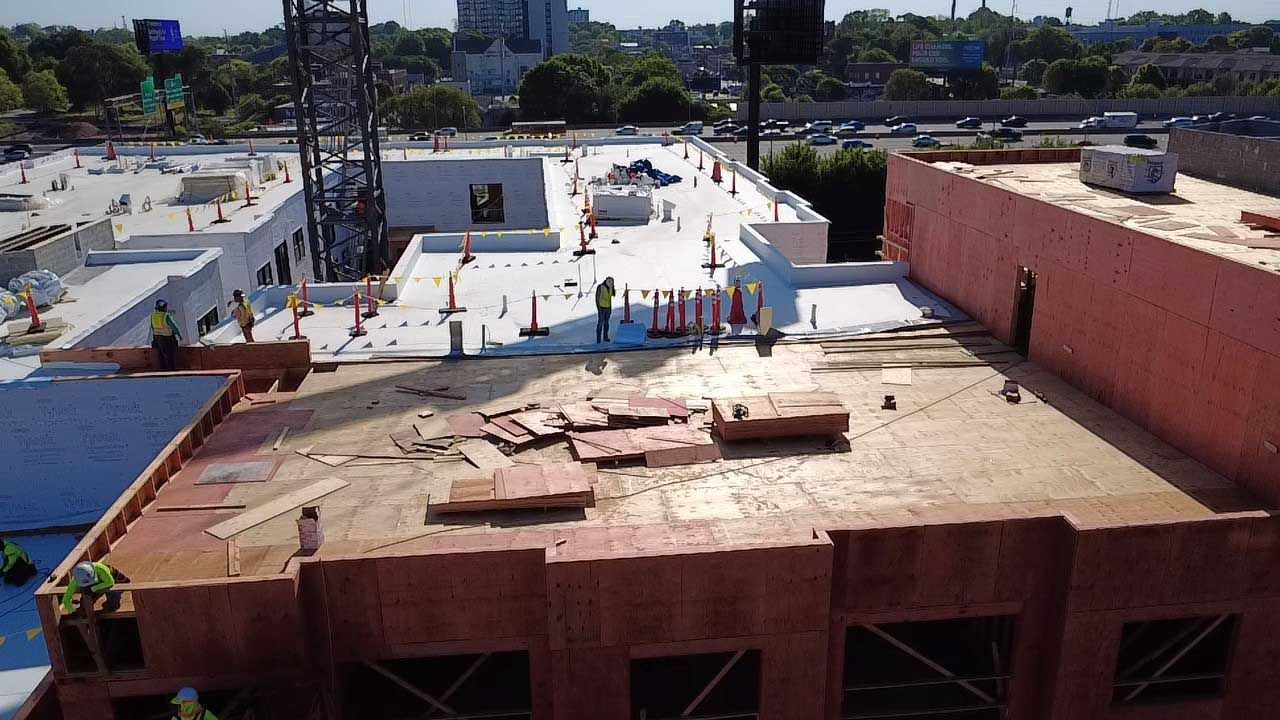 Rooftop construction site with workers on a white roof beside a red building under a clear sky