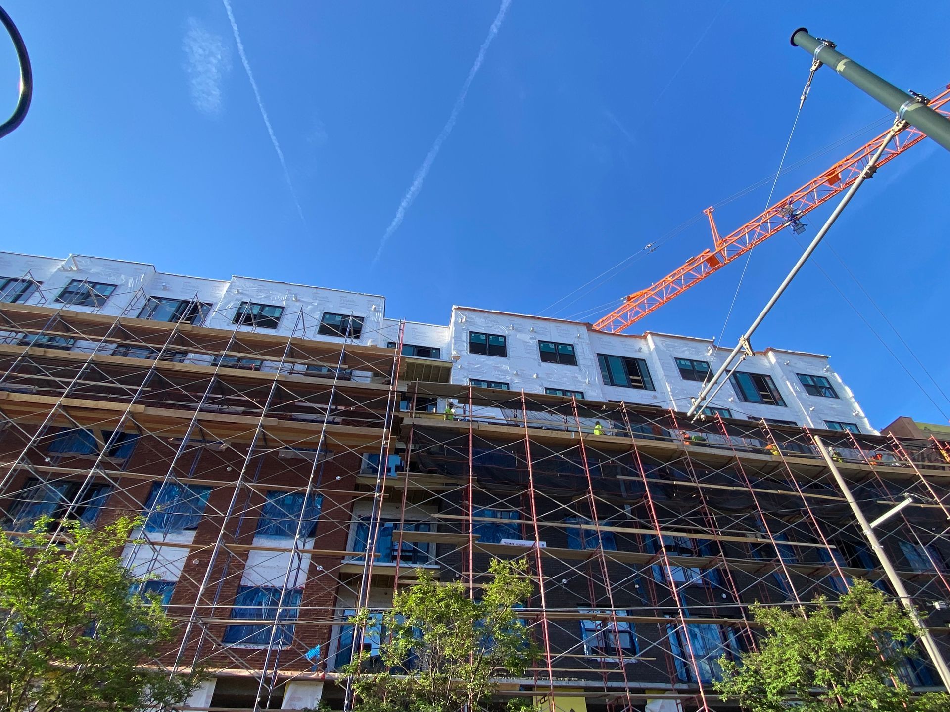 Scaffolded building under construction with an orange crane against a clear blue sky