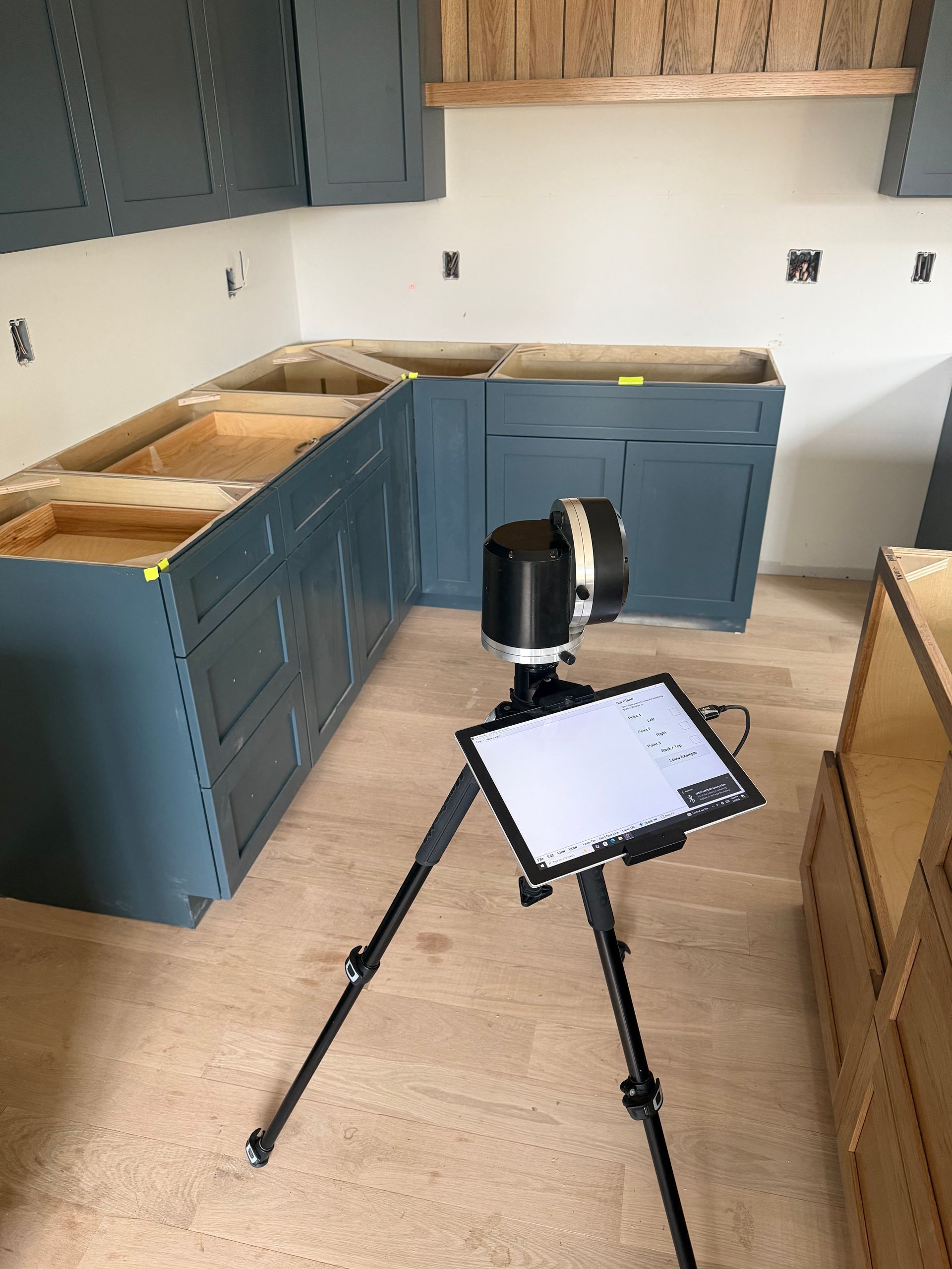 A digital laser templating device on a tripod scanning blue kitchen cabinets during a home renovation.