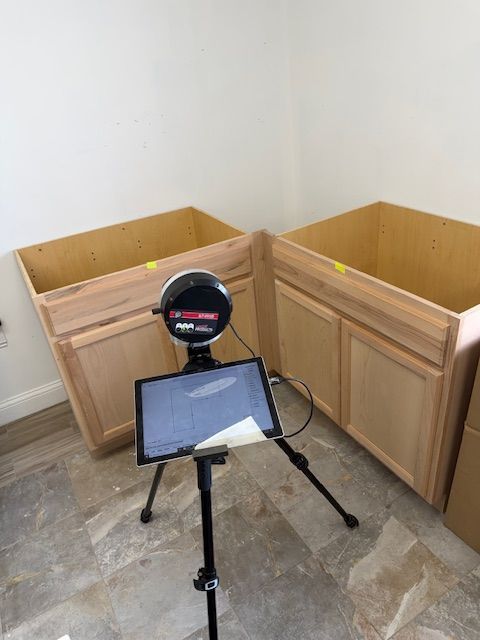 Cabinets with a tablet on a tripod, likely for measurement or inspection, in a room.