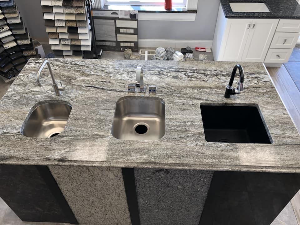Granite countertop with three sinks and faucets in a showroom.