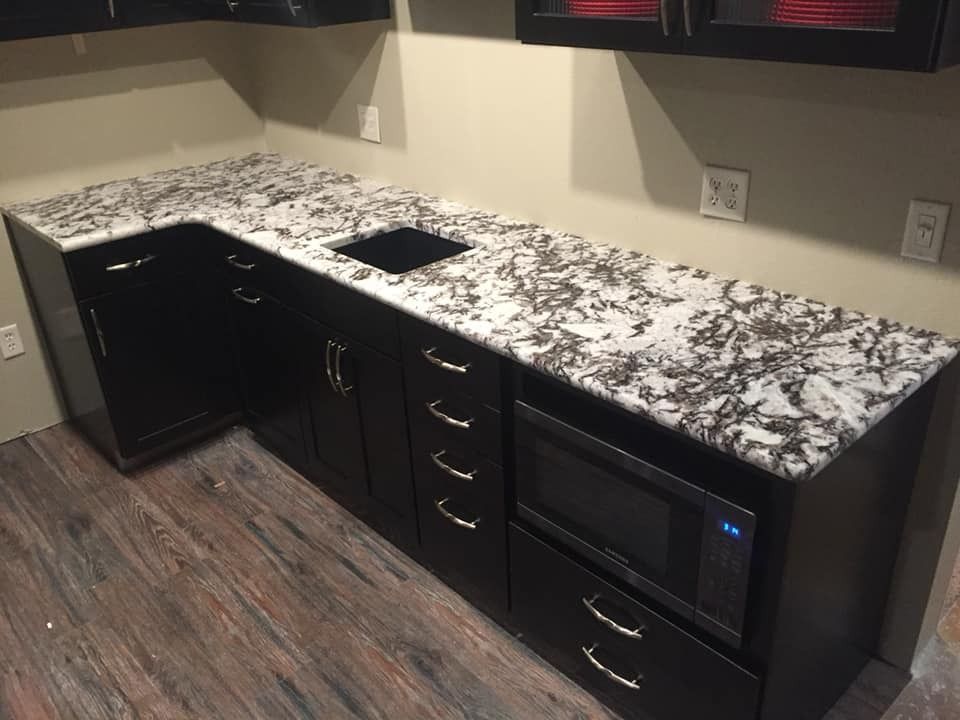 Black cabinets with granite countertop, microwave, and sink in a kitchen setting.