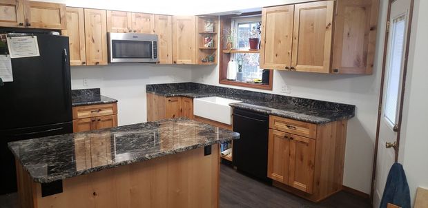 Kitchen with wooden cabinets, black appliances, dark countertops, and a white farmhouse sink.