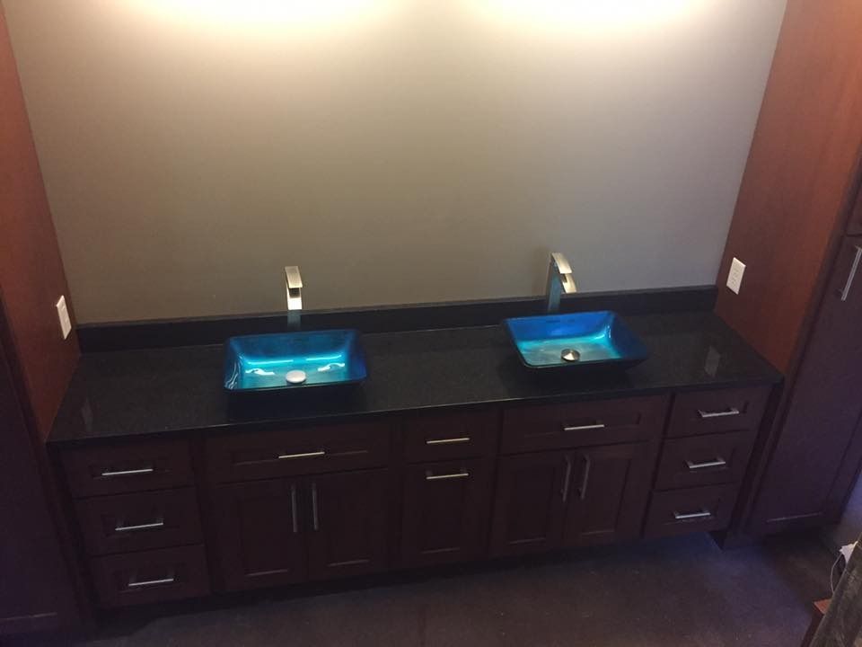 Two sinks with blue glass bowls on a dark countertop and dark brown cabinets.