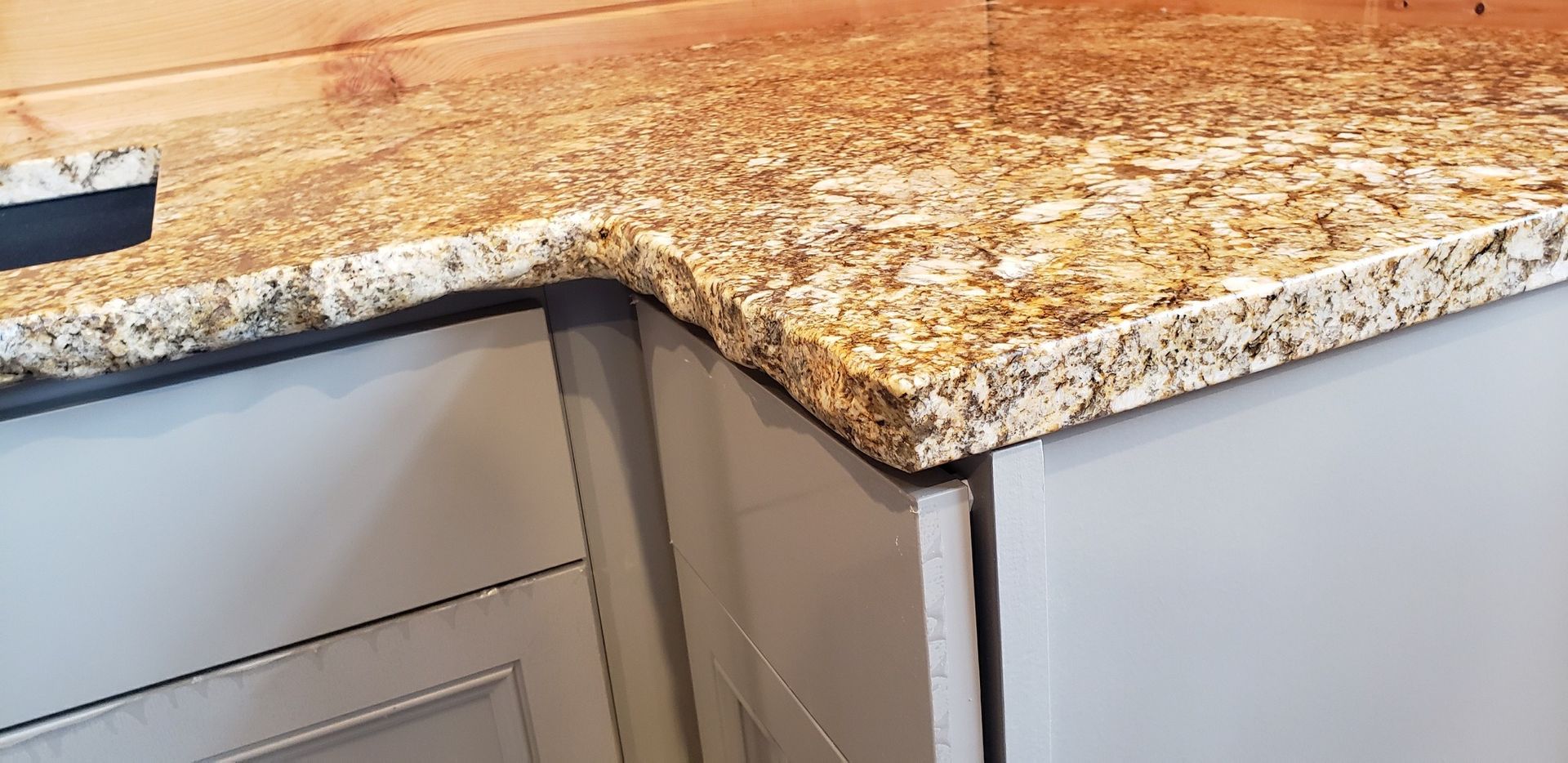Granite countertop with a curved edge on light gray cabinetry.