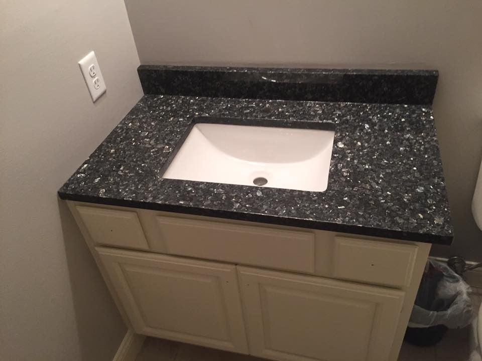 Bathroom vanity with a dark speckled countertop, white sink, and cream-colored cabinet.