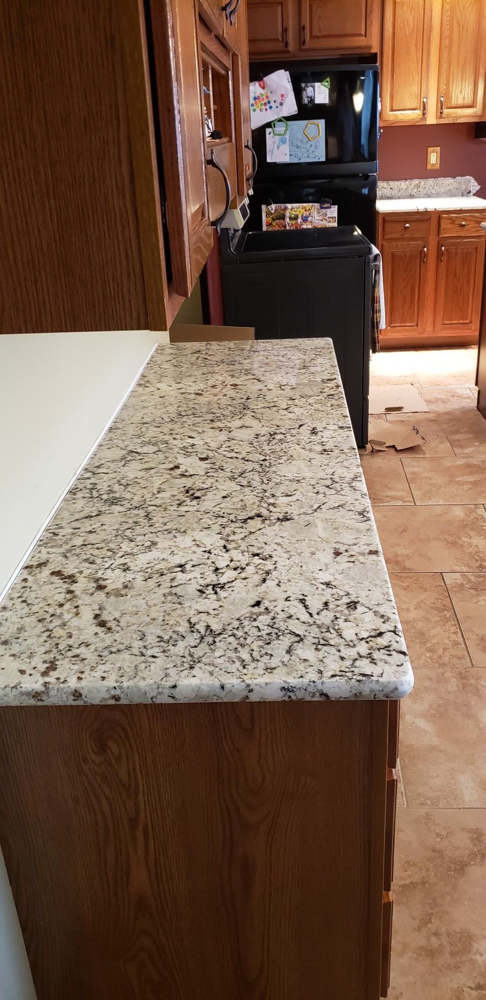 Kitchen countertop with beige granite and brown cabinets. Black appliances are in the background.