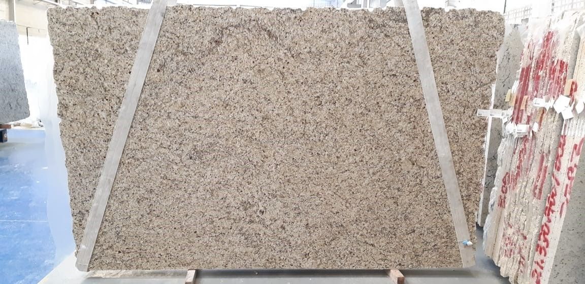 A large, rectangular granite slab is being lifted by straps. The granite is beige with dark spots.