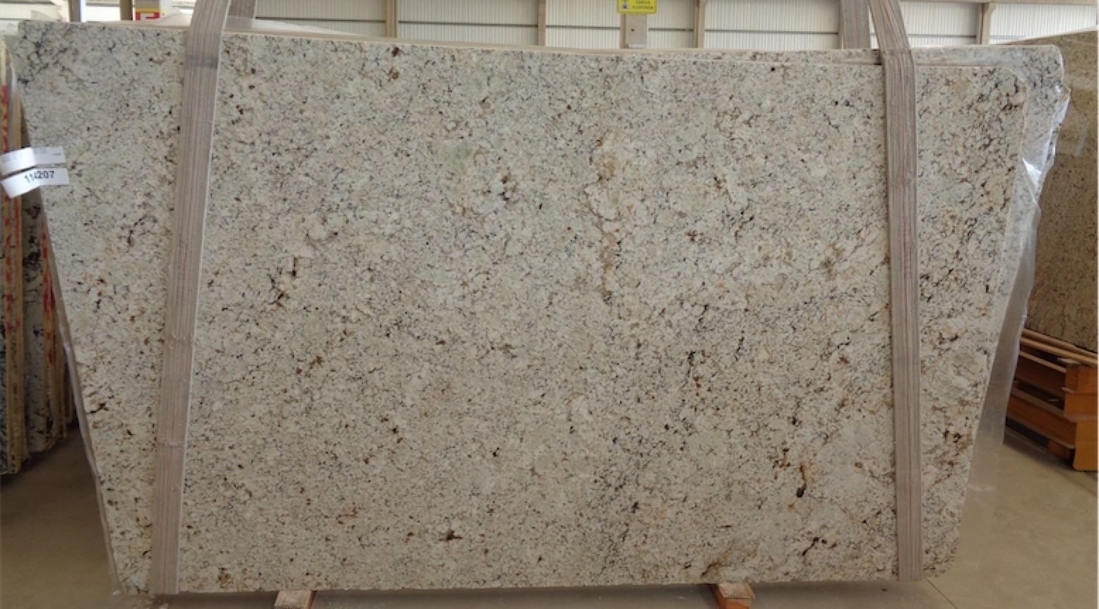 Large granite slab with light beige and brown speckles, wrapped in plastic, ready for transport.