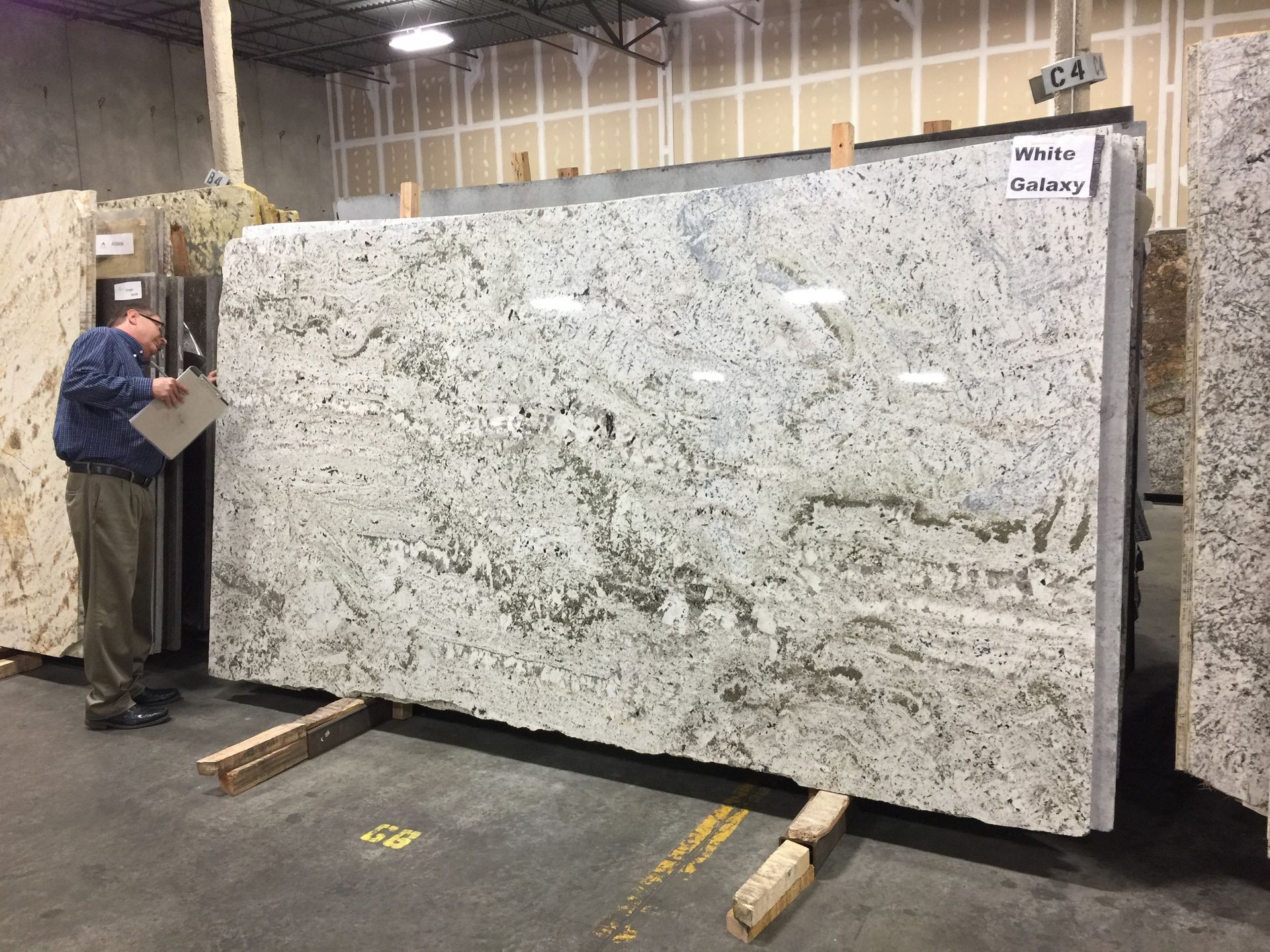 Man inspecting large white granite slab with gray and gold veining in a warehouse.