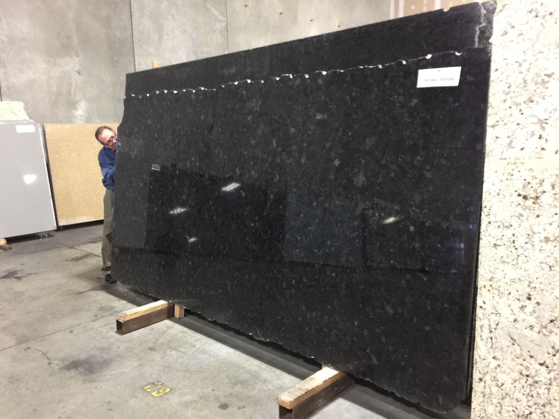 Large black granite slab propped up in a warehouse, with a person inspecting it.