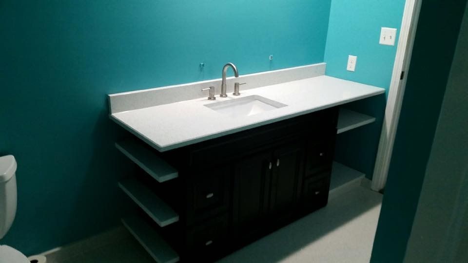 Bathroom vanity with a dark cabinet, white countertop, and turquoise walls. Shelves on the side.