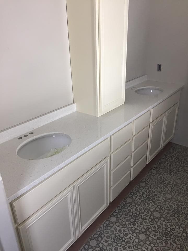 Bathroom vanity with dual sinks, cream cabinets, and quartz countertop. Tall cabinet sits between the sinks.