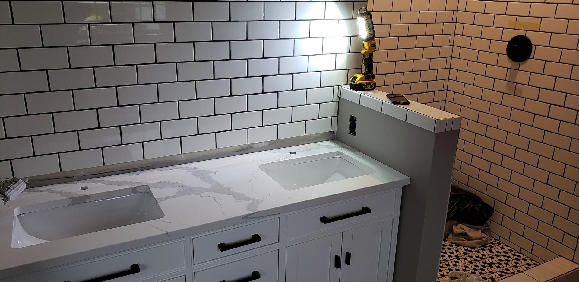 White-tiled bathroom with a white vanity and a shower, black hardware.