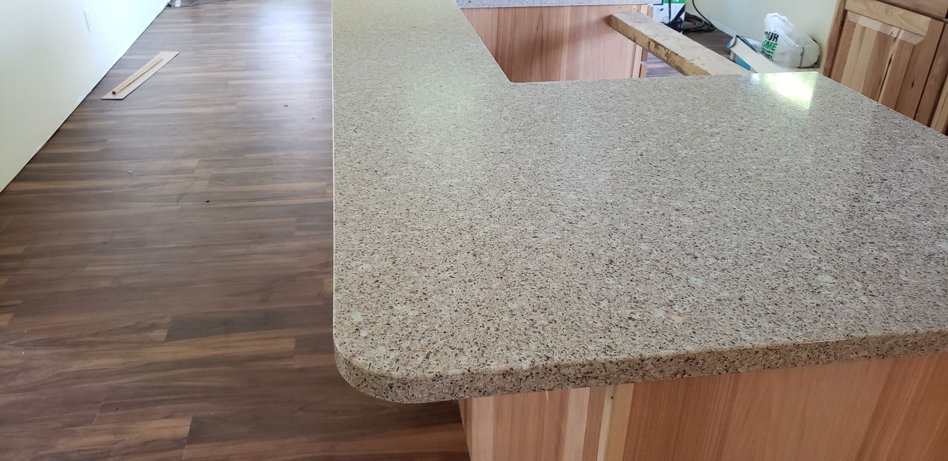 Kitchen countertop with speckled surface and wooden cabinets and flooring.