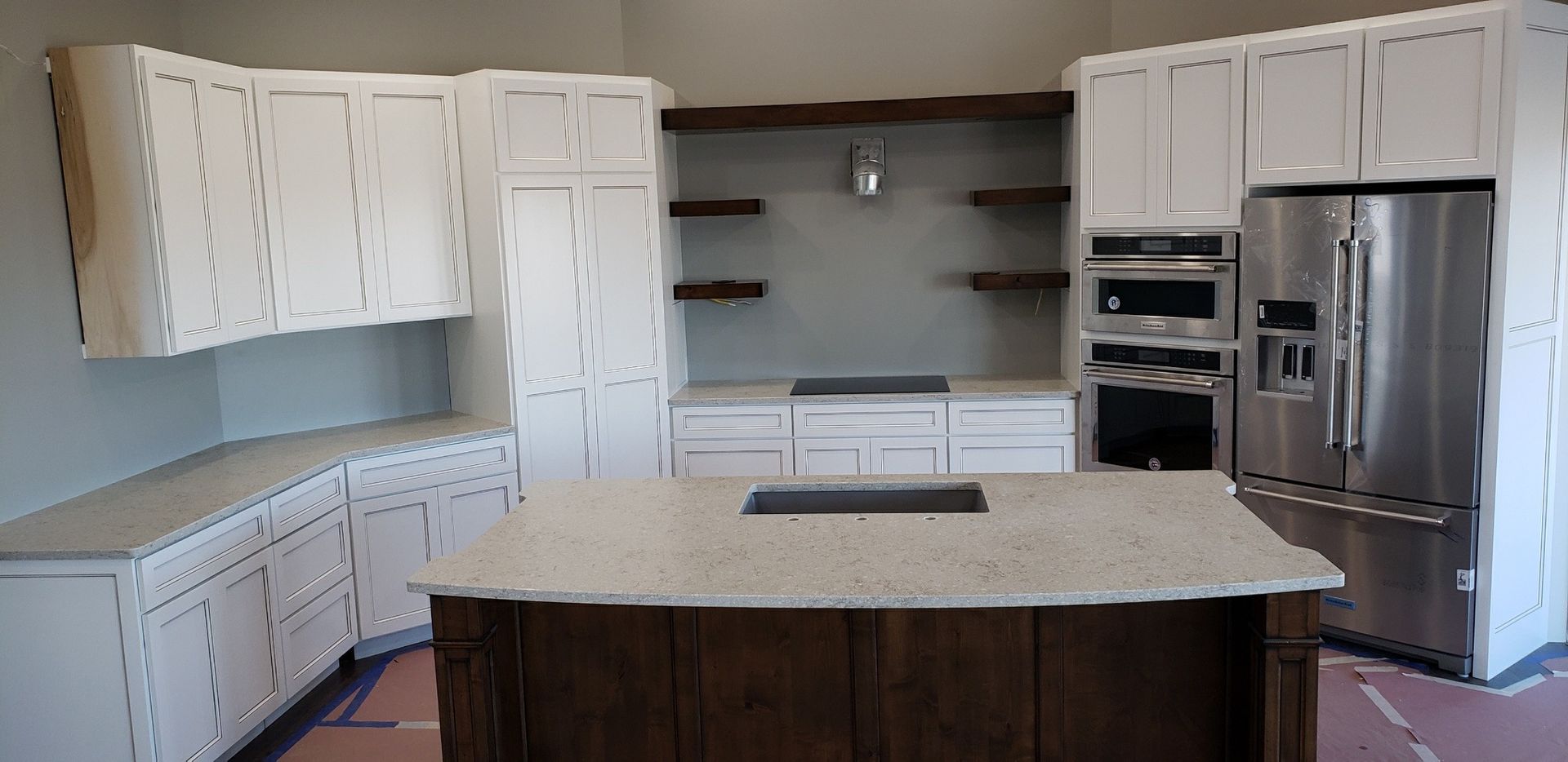 A kitchen with white cabinets, stainless steel appliances, and a dark brown island.