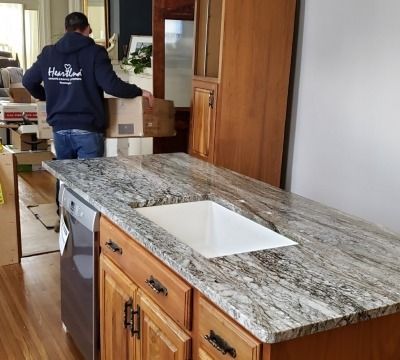Kitchen with granite countertop, sink, dishwasher, and cabinets. A person in a blue hoodie moves boxes in the background.