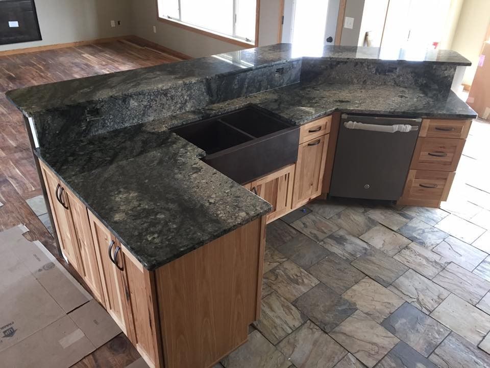Kitchen island with granite countertop, wood cabinets, and built-in sink and dishwasher.
