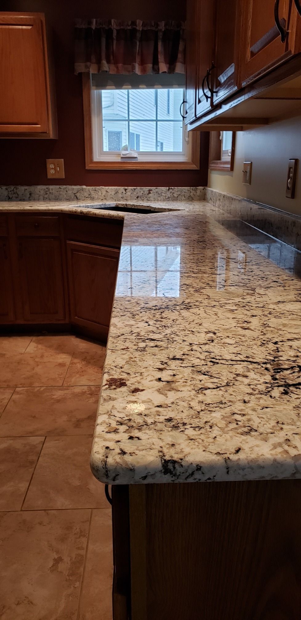 Granite kitchen countertop reflecting window light. Wooden cabinets and a window are visible in the background.
