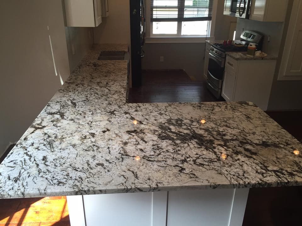 L-shaped kitchen countertop with white cabinets and speckled granite. Sunlight streams in from a window.