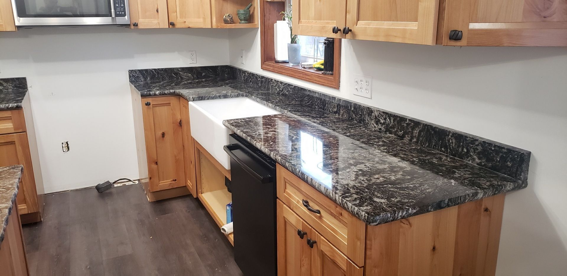 Kitchen with light wood cabinets and dark countertops, farmhouse sink, and dishwasher.
