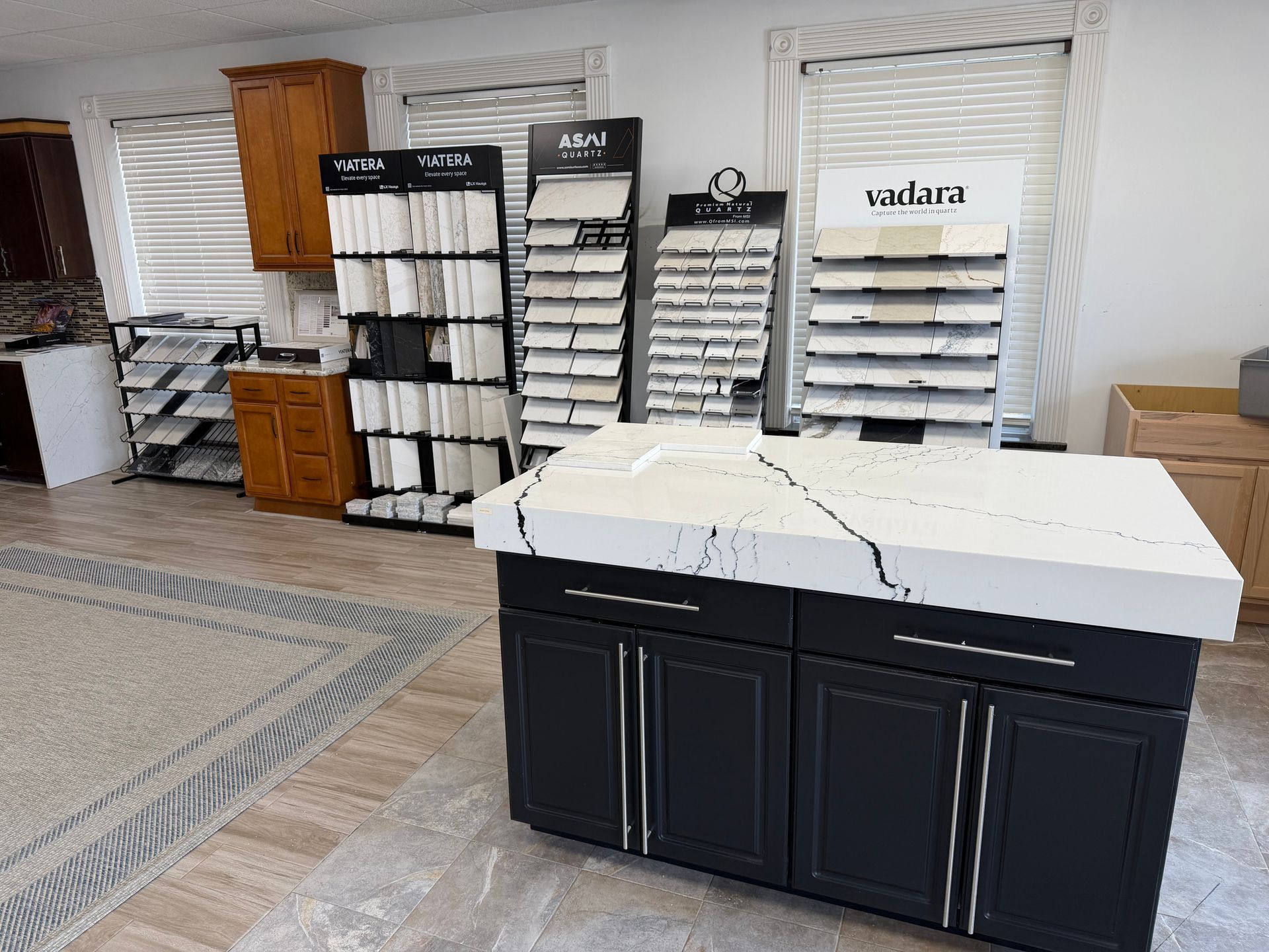 A showroom displays stone countertop samples on shelves and a black island with a white marble-patterned countertop.