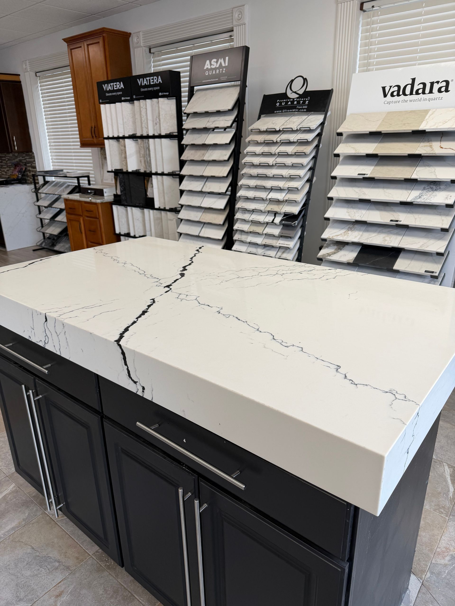 A showroom displaying stone countertop samples with a large, white, veined quartz island in the foreground.